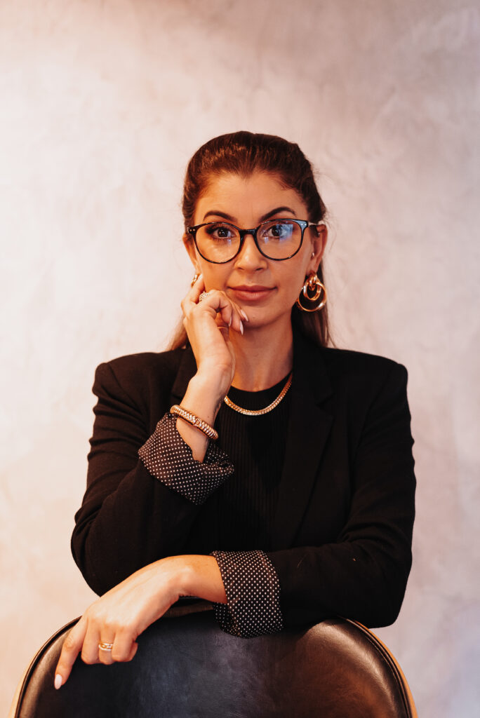 A advogada Mariana Rieping de roupa preta de manga longa apoiada em uma cadeira e com uma mão no rosto, com fundo claro
